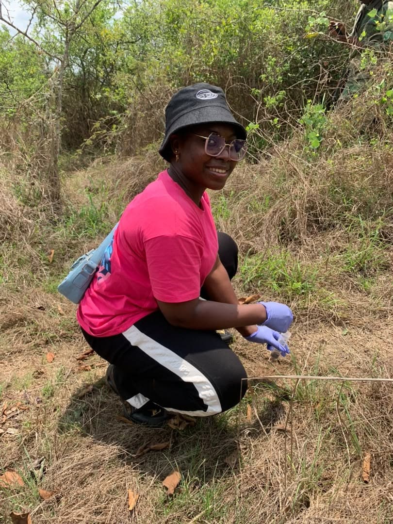 Researcher crouching in grassland to collect a soil sample