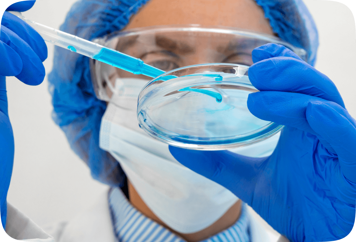 Scientist in a mask and goggles pipetting blue liquid into a petri dish
